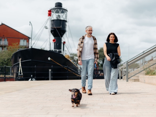 A man and a woman walk their dog in front of a large boat