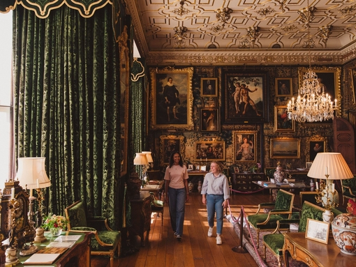 Two women walk through an ornate room in a heritage house