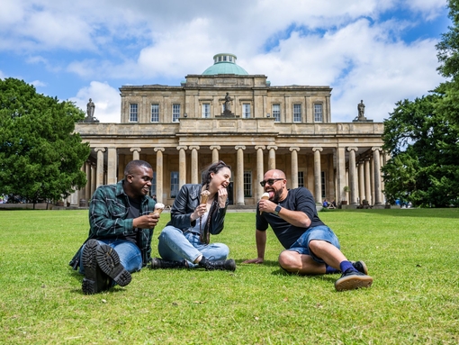 Deux hommes et une femme sont assis sur l'herbe à l'extérieur d'un bâtiment historique.