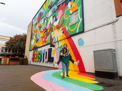 Two people playfully smiling and posing in front of a colourful mural
