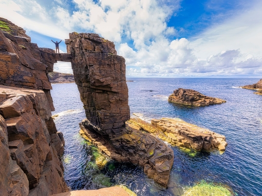 Man straddling two sea stacks overlooking a rocky outcrop and the ocean