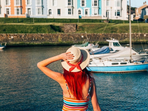 A girl sitting on the wall of a harbour looking at the boats