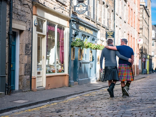 Gleichgeschlechtliches männliches Paar in Schottenröcken geht Arm in Arm