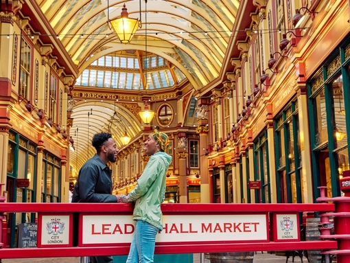 ثنائي مبتسم يتبادل الحديث أمام قاعة سوق ذات سقف ذهبي مزخرف بإتقان.