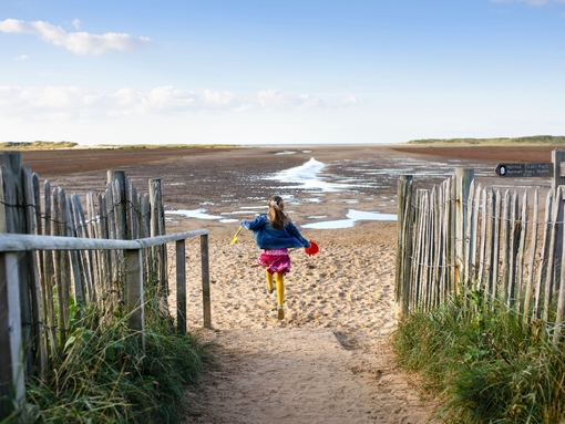A girl running down a path to Holkham Beach