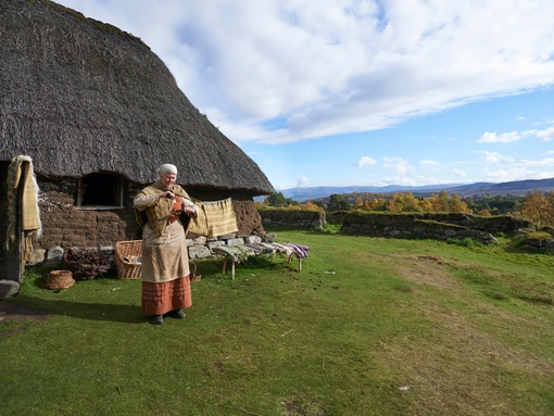 Femme en tenue traditionnelle devant une maison du Highland Folk Museum.