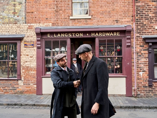 Two men shaking hands on the street in front a hardware shop at a living museum