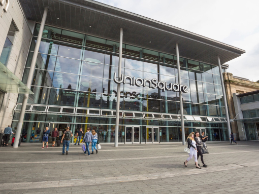People carrying bags of shopping walking around outside of a modern shopping centre. 