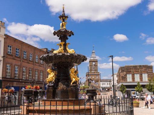 An ornate black and gold fountain with statues of people and fish in the centre of a shopping street.