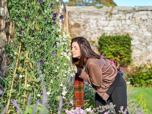 A woman smelling flowers in the gardens of a castle