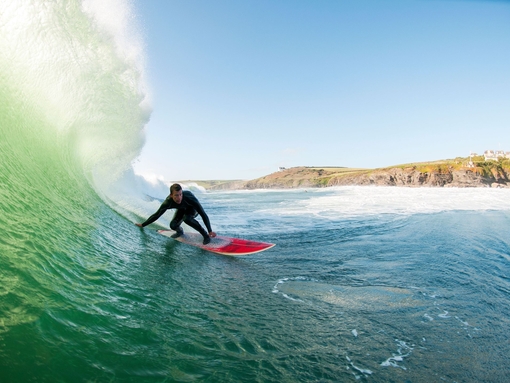 Surfer in a wetsuit surfing a large wave on a red surfboard