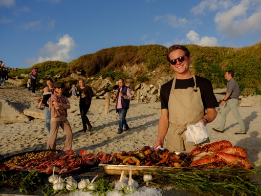 A man posing behind a row of barbeque food at Taste of Scilly Food Festival on Tresco Island