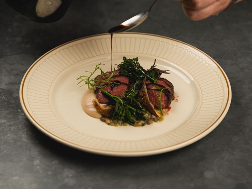 Hand pouring sauce over a steak dish