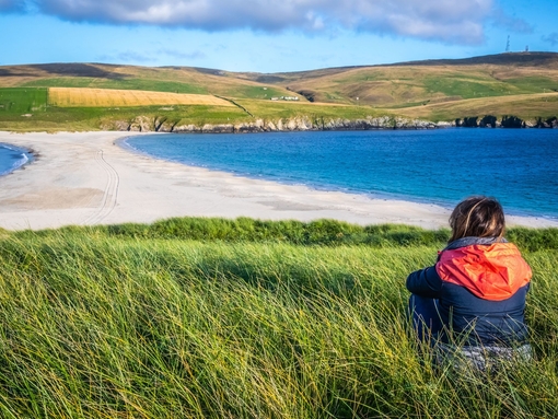 A woman sitting in grass overlooking a spit and fields