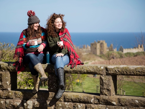 Women holding mugs with hot drinks, sitting on a stone wall