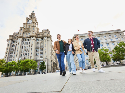 أربعة أصدقاء يستكشفون مدينة محلية وهم يتمشون على ممشى الواجهة البحرية، وخلفهم مبان تاريخية.