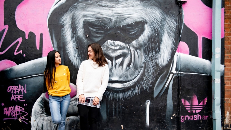 Two women standing in front of painted mural on street wall