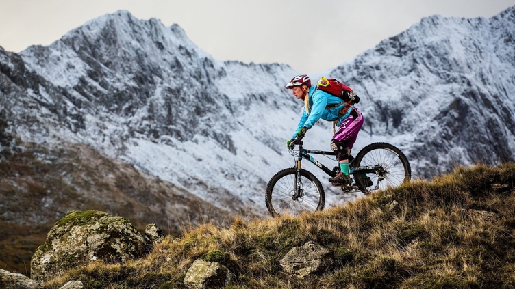Mountain biker rolling down a slope. Mountain backdrop