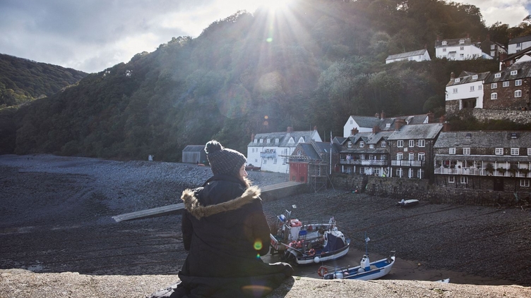 Woman sitting on harbour wall looking down on orw boats