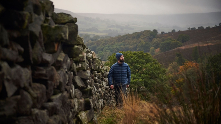A man walking beside a dry stone wall with a valley view