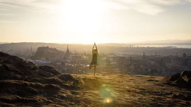 Young woman doing yoga on a hill overlooking a city