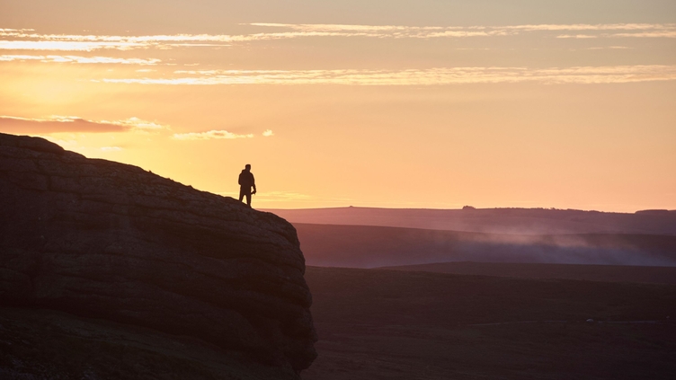 Silhouette of person hiking on large hill at sunset