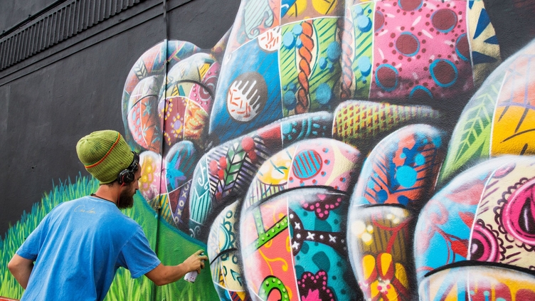 Man with a can working on a colourful artwork on wall