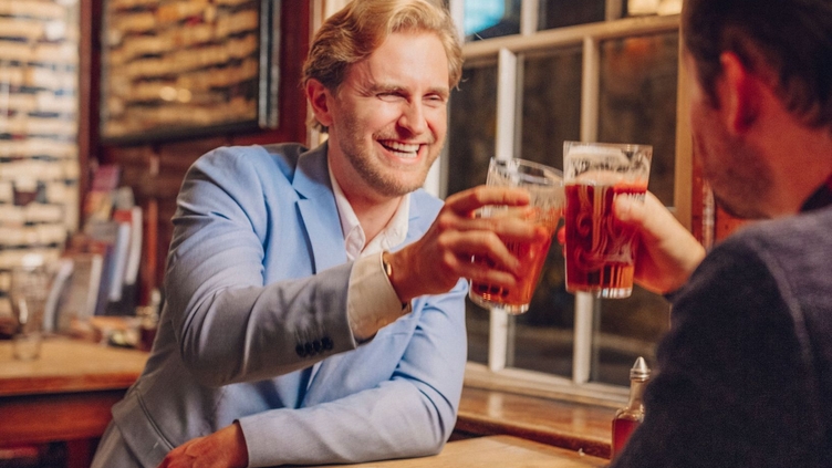 Two men toasting with pints in a bar in the evening