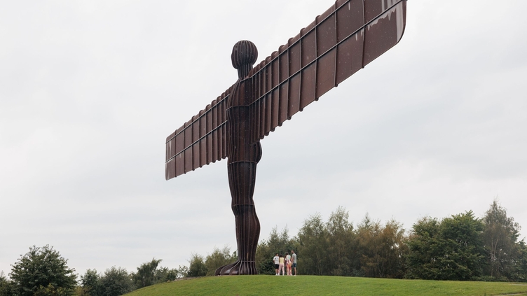 Trois personnes posant près d'une sculpture géante en acier