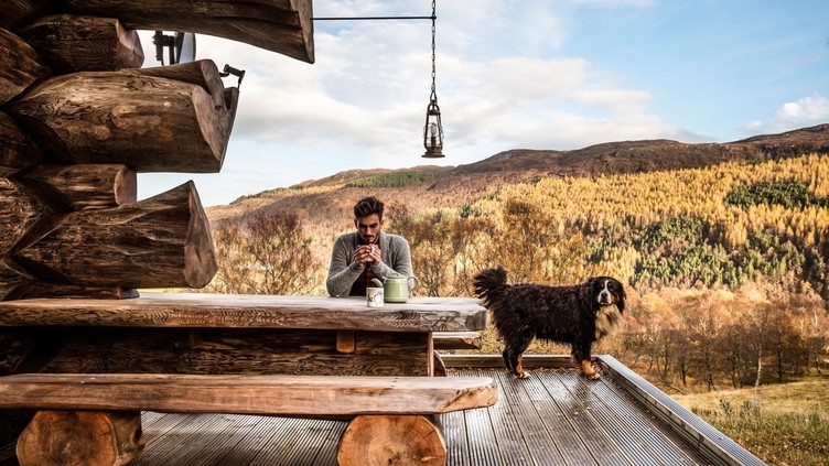 Man sitting on the terrace of a wooden lodge with large St Bernard dog, Scottish Highlands