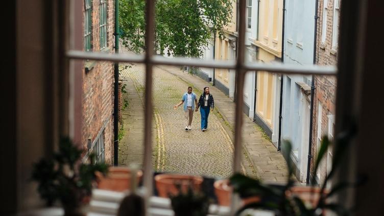 A man and a woman walk along a cobbled street seen through a window