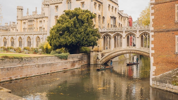 People punting on the river under a bridge in front of an historical building
