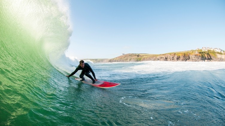 Surfer in a wetsuit surfing a large wave on a red surfboard