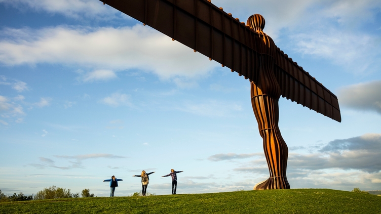 Three people posing near a giant steel sculpture