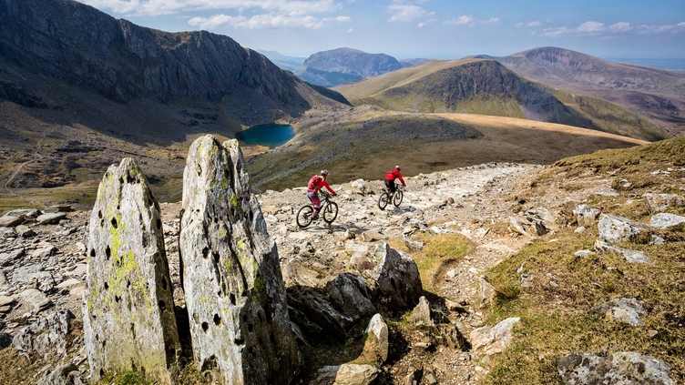 Two mountain bikers riding on the stoney path. Lake ahead