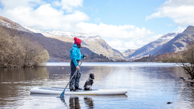 Woman and dog on a paddle-board on lake near mountains