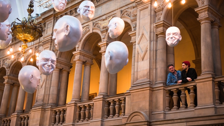 Two men looking at installation of suspended head sculptures