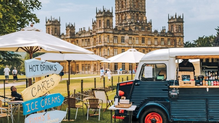 Food truck and direction signs at a festival at Highclere Castle with house behind