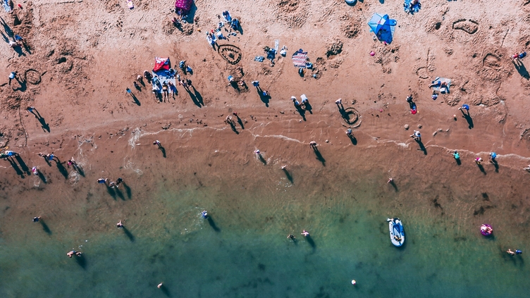 Aerial view of people on sandy beach and swimming in sea