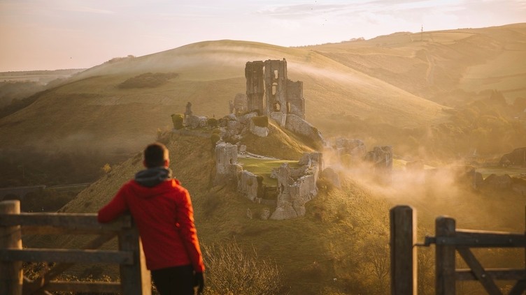 Man leaning on gatepost, looking out to views of castle