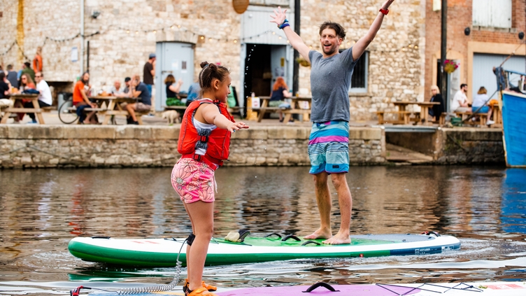 A child and a man stood on paddleboards in the River Exe in Exeter