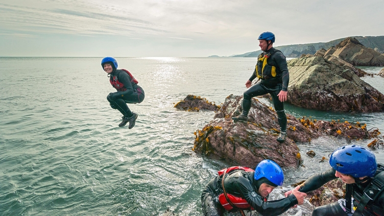 People coasteering off rocks into the ocean.