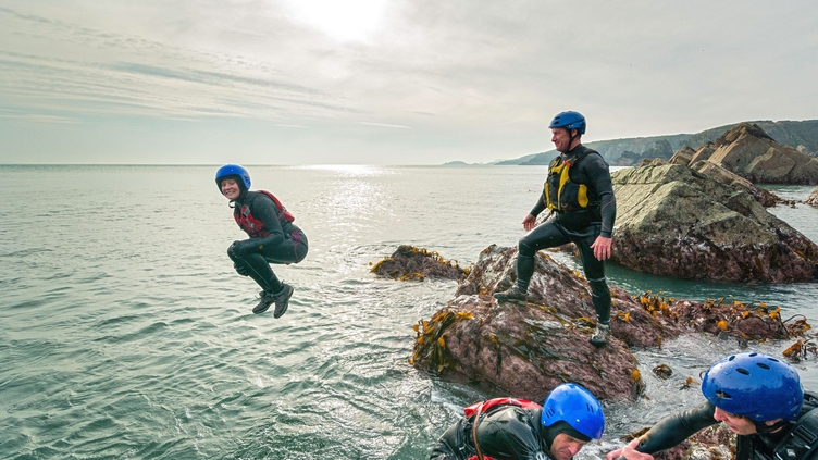 People coasteering off rocks into the ocean.