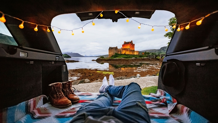 Man lying in camper van looking at castle in distance