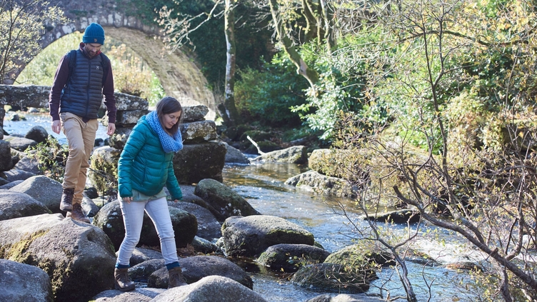 Couple balancing on boulders by a stream near trees