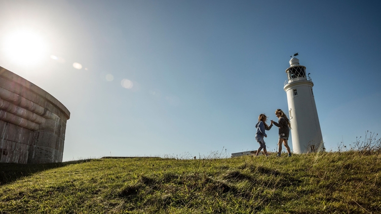 Two children playing in open space by a lighthouse