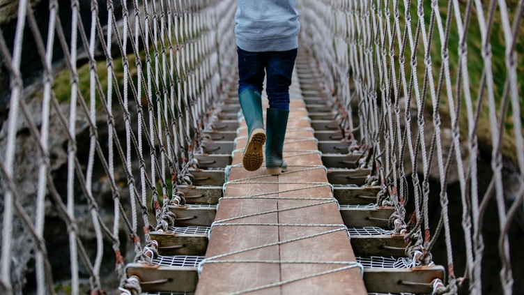 Young boy crossing a long rope bridge. Rear view