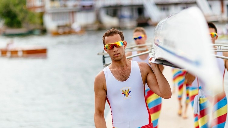 Rowers, wearing striped shorts, carrying racing shell