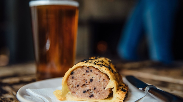Close up of pint of beer and plate with sausage roll