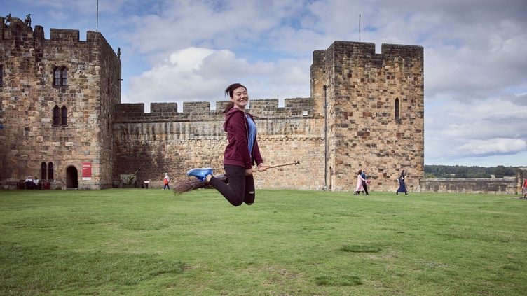 Young woman hovering on a broomstick in the Outer Bailey of Alnwick Castle